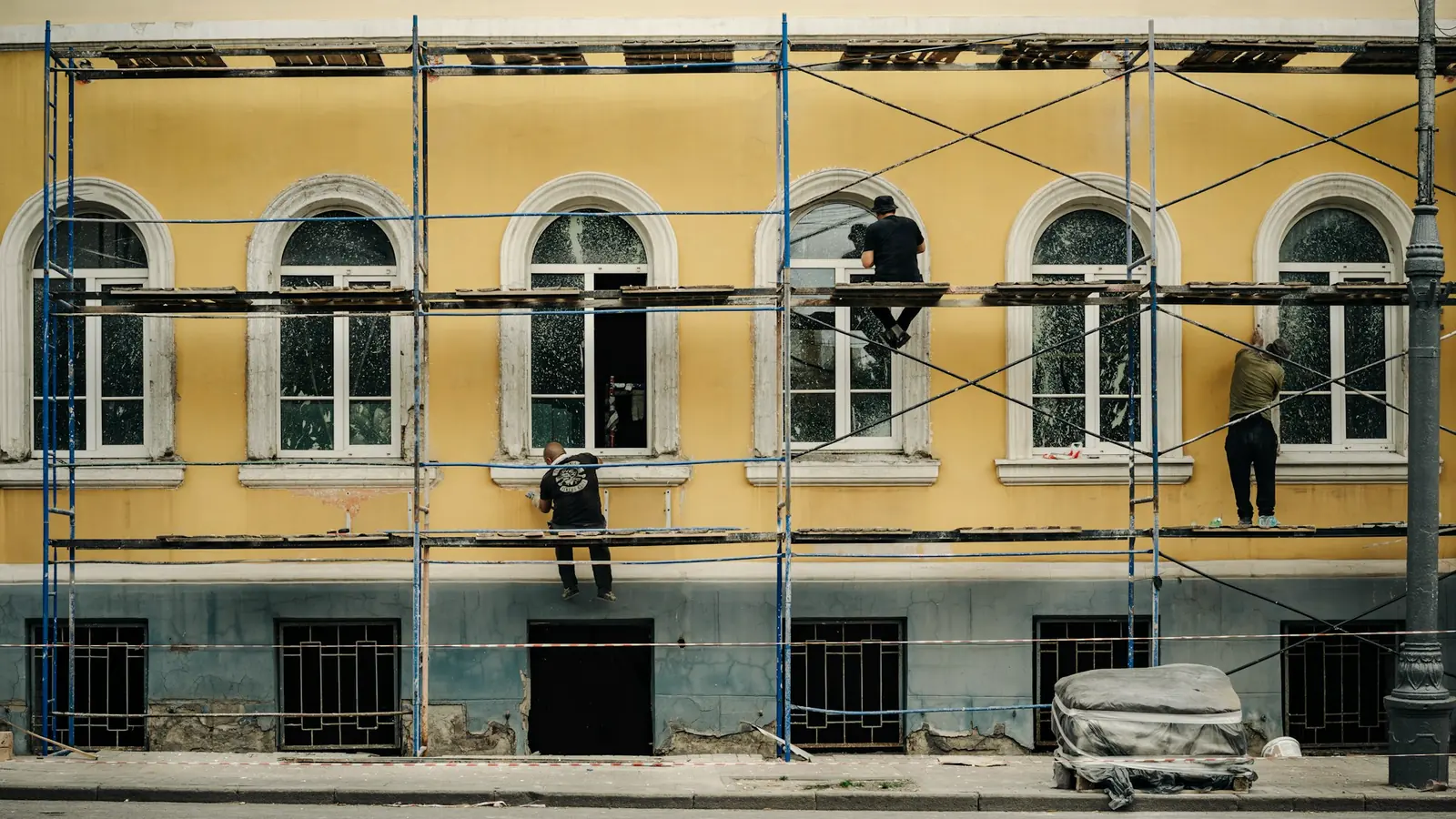 Fachada com janelas em arco em reabilitação, com andaime e trabalhadores (fotografia ilustrativa)